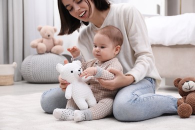 Cute baby and mother playing with toy bear on floor at home