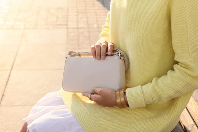 Fashionable woman with stylish bag on bench outdoors, closeup