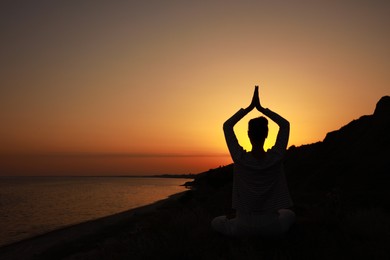 Photo of Woman meditating near sea at sunset, back view. Space for text