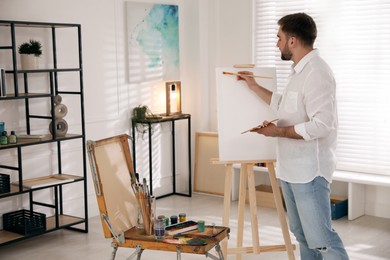 Young man painting on easel with brush in artist studio