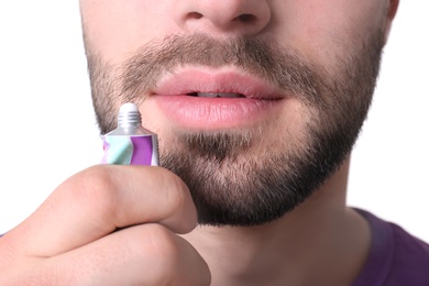 Young man applying cold sore cream on lips against white background, closeup