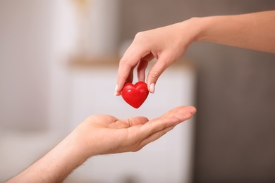 Woman giving red heart to man on blurred background, closeup. Donation concept