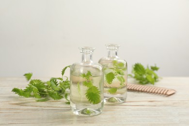 Photo of Stinging nettle, extract and comb on white wooden background. Natural hair care