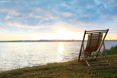Photo of Empty wooden deckchair on hill near calm river