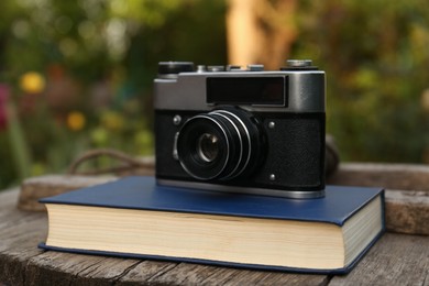 Photo of Hardcover book and vintage camera on wooden table outdoors