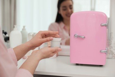 Woman getting ready at dressing table with cosmetic refrigerator indoors, closeup