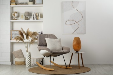 Soft rocking chair with pillow on rug near wall in room. Interior design