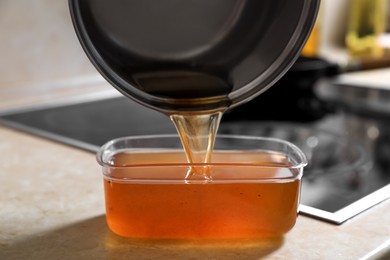 Pouring used cooking oil from saucepan into container on kitchen counter, closeup