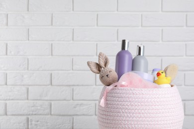 Basket full of different baby cosmetic products, accessories and toys against white brick wall. Space for text
