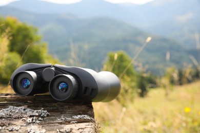 Modern binoculars on wooden log outdoors, space for text
