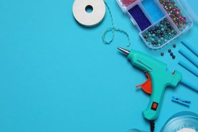 Hot glue gun and handicraft materials on light blue background, flat lay. Space for text