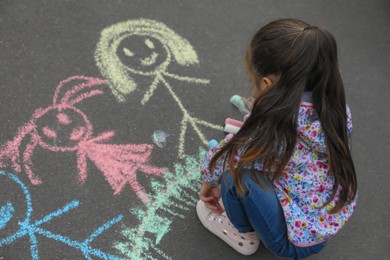 Child drawing family with chalk on asphalt