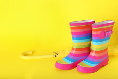 Pair of striped rubber boots near umbrella on yellow  background. Space for text