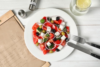 Plate with delicious Greek salad and menu on table, top view