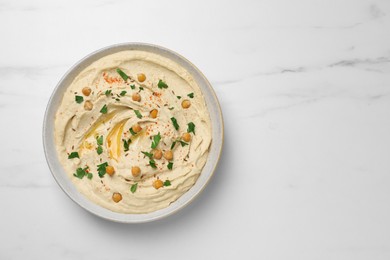 Tasty hummus with garnish in bowl on white marble table, top view. Space for text