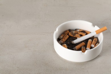 White ceramic ashtray with cigarette butts on grey table. Space for text