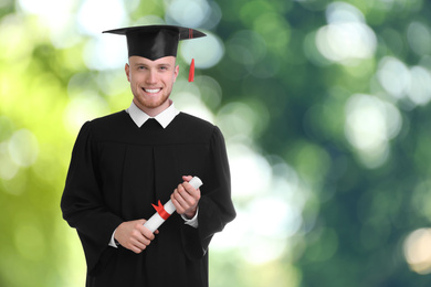 Happy student with graduation hat and diploma on blurred background, space for text