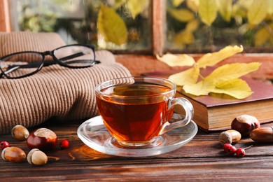 Photo of Cup of aromatic tea, book and soft sweater on wooden windowsill indoors. Autumn atmosphere