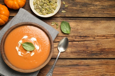 Tasty creamy pumpkin soup with basil in bowl on wooden table, flat lay. Space for text