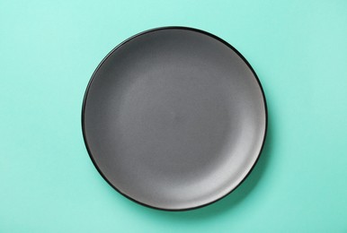 Empty grey ceramic plate on turquoise background, top view