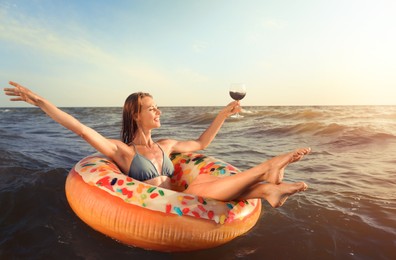 Happy woman with glass of wine and inflatable ring in sea