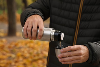 Man pouring drink from thermos into cap outdoors, closeup
