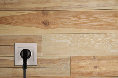 Wooden wall with power socket and inserted plug, space for text. Electrical supply
