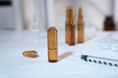 Open pharmaceutical ampoule with medication and syringe on white wooden table