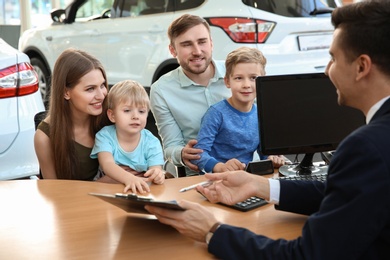 Young family with salesman sitting at table in dealership. Buying new car