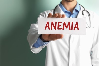Doctor holding sign with word ANEMIA on color background, closeup