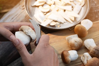 Man cutting mushroom with knife at wooden table, closeup