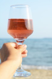 Photo of Woman holding glass of tasty rose wine near sea, closeup