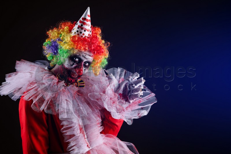 Photo of Terrifying clown on dark background, space for text. Halloween party costume