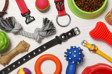 Flat lay composition with dog collars, toys and food on white wooden table