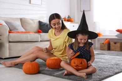 Mother and daughter making pumpkin jack o'lanterns at home. Halloween celebration
