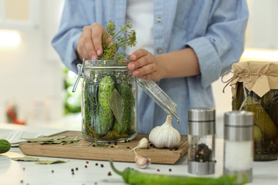 Woman putting dill into pickling jar at table in kitchen, closeup