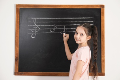 Little girl writing music notes on blackboard in classroom