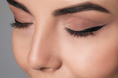 Beautiful woman with black eyeliner on grey background, closeup