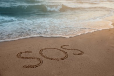 SOS message drawn on sandy beach near sea