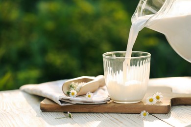Pouring tasty fresh milk from jug into glass on white wooden table, closeup. Space for text