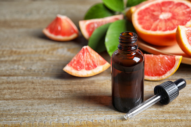 Citrus essential oil and grapefruits on wooden table. Space for text