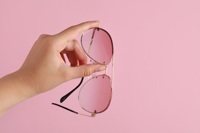 Photo of Woman holding stylish sunglasses on pink background, closeup of hand. Space for text