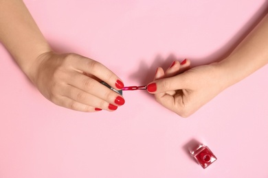 Woman applying nail polish on color background, top view