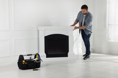 Man installing electric fireplace near white wall in room
