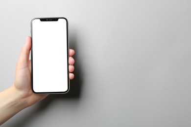 Photo of Woman holding smartphone with blank screen on grey background, closeup. Mockup for design