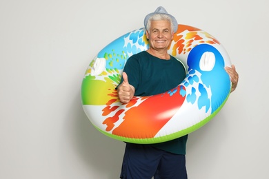 Funny mature man with bright inflatable ring on light background