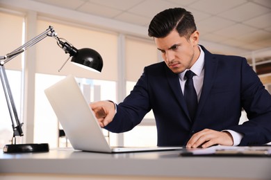 Emotional businessman with laptop at table in office