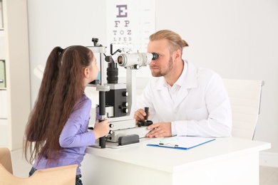 Children's doctor examining little girl with ophthalmic equipment in clinic