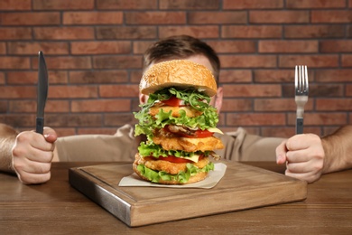Photo of Hungry man with cutlery eating huge burger at table
