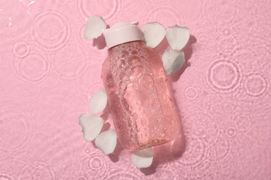 Photo of Wet bottle of micellar water and petals on pink background, top view